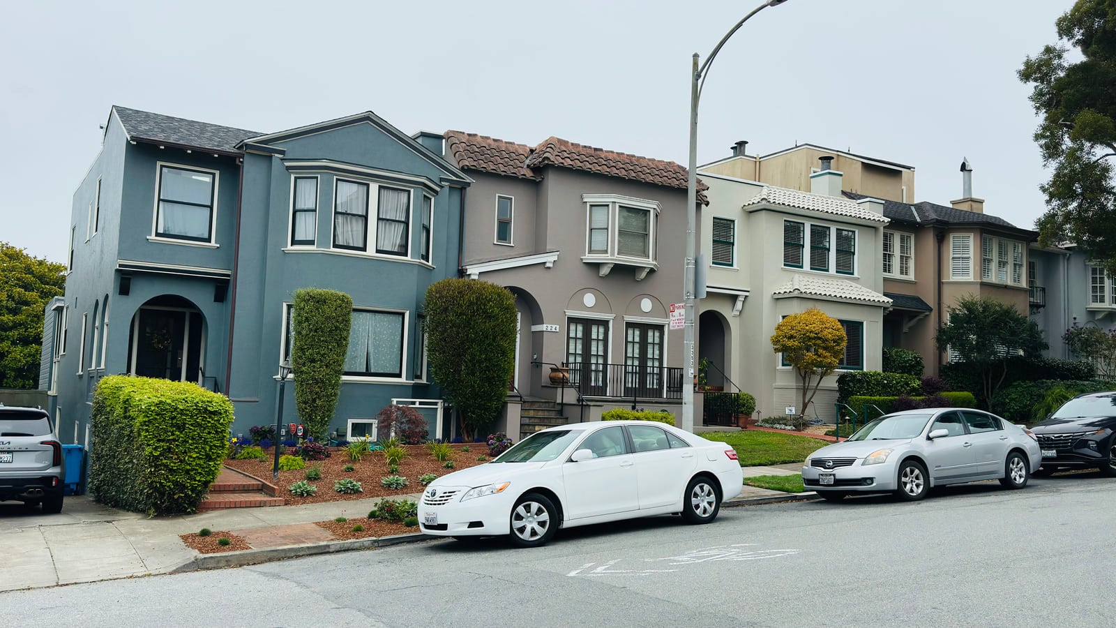 A row of pale blue and grey Edwardian houses along a level street with cars parked outside.