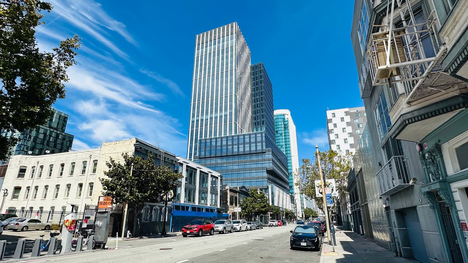 A SoMa street of low buildings running toward a glass tower rising downtown.