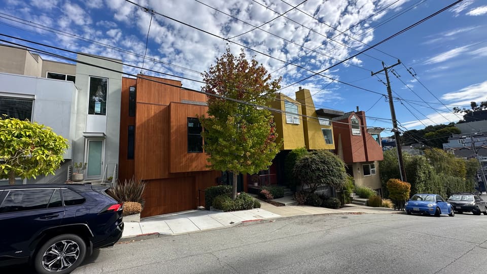 Modern Bernal Heights infill houses in corten steel and yellow render on a sloping residential street.