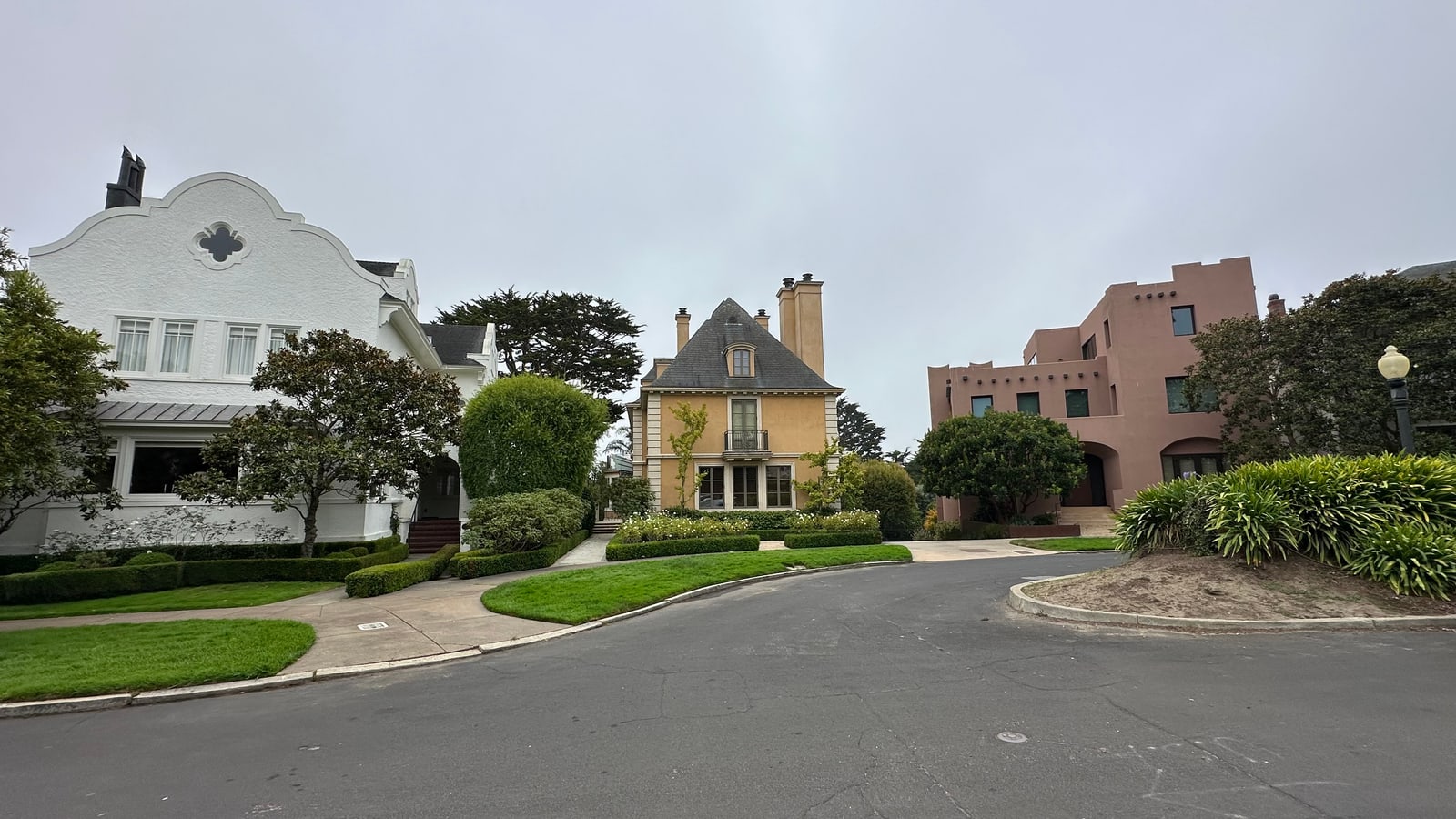 Shingled and pink stucco houses arranged around a circular street island in Presidio Heights.