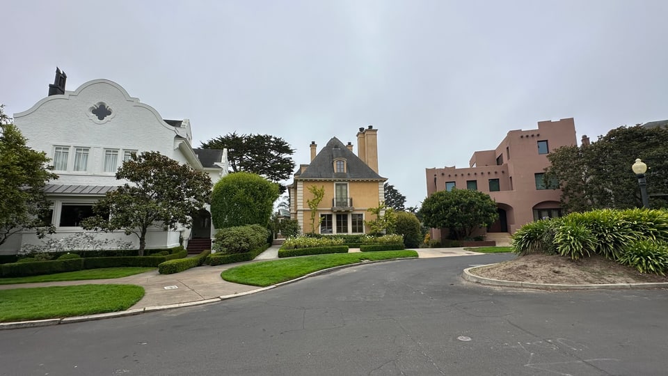Shingled and pink stucco houses arranged around a circular street island in Presidio Heights.