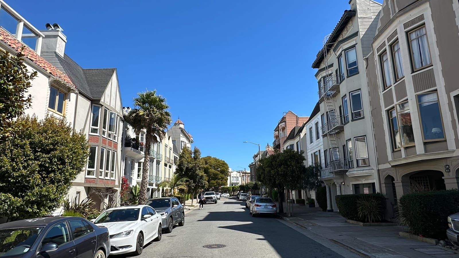 A Marina district street of white and cream homes sloping toward the bay, palms along the sidewalk under a clear sky.