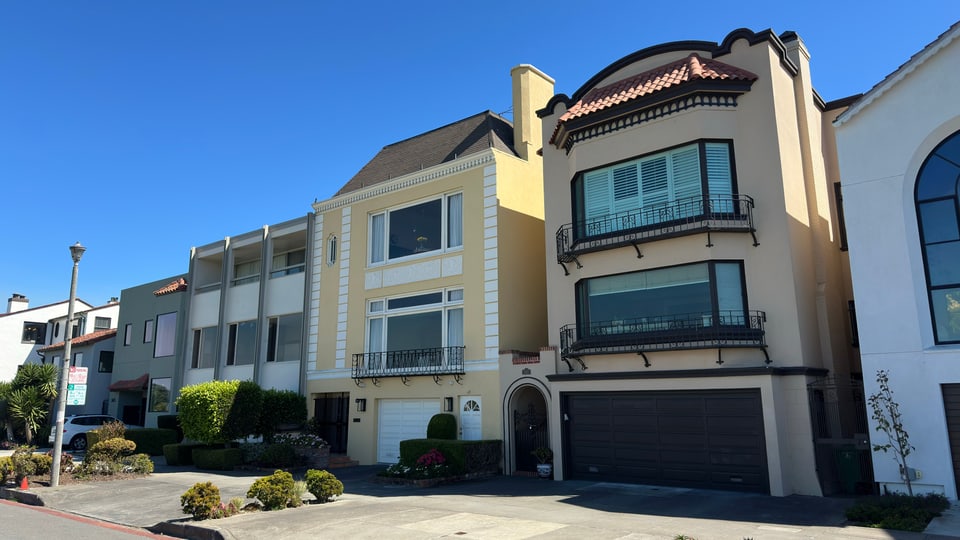 A Marina district street of white and cream homes sloping toward the bay, palms along the sidewalk under a clear sky.