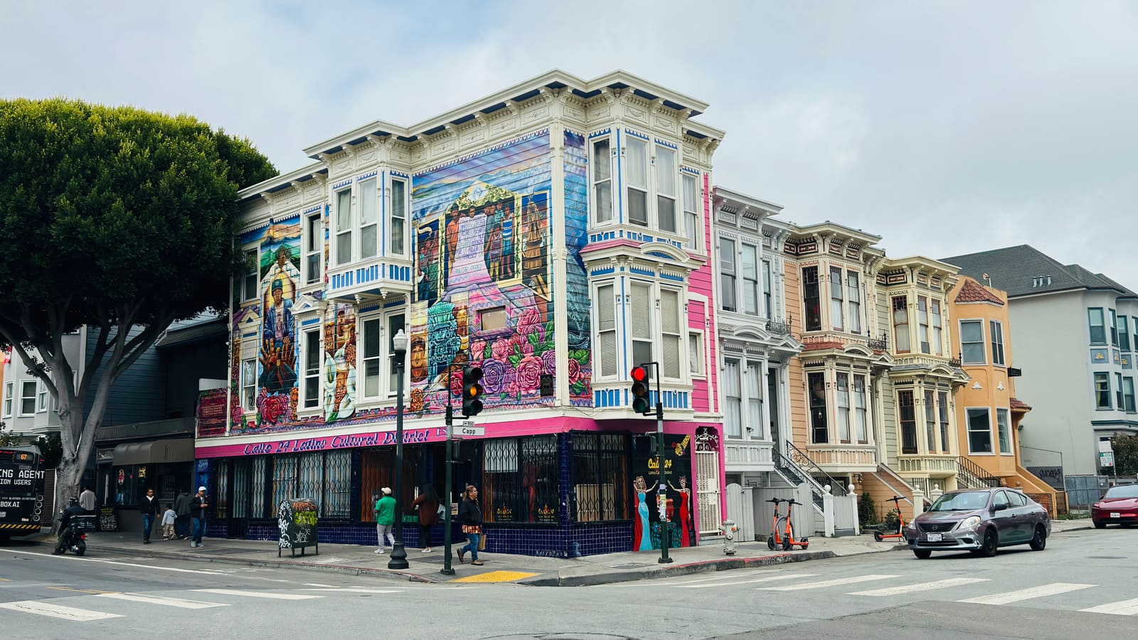 A muralled corner Victorian on Valencia Street in San Francisco's Mission District, with a row of Victorian facades receding up the block.