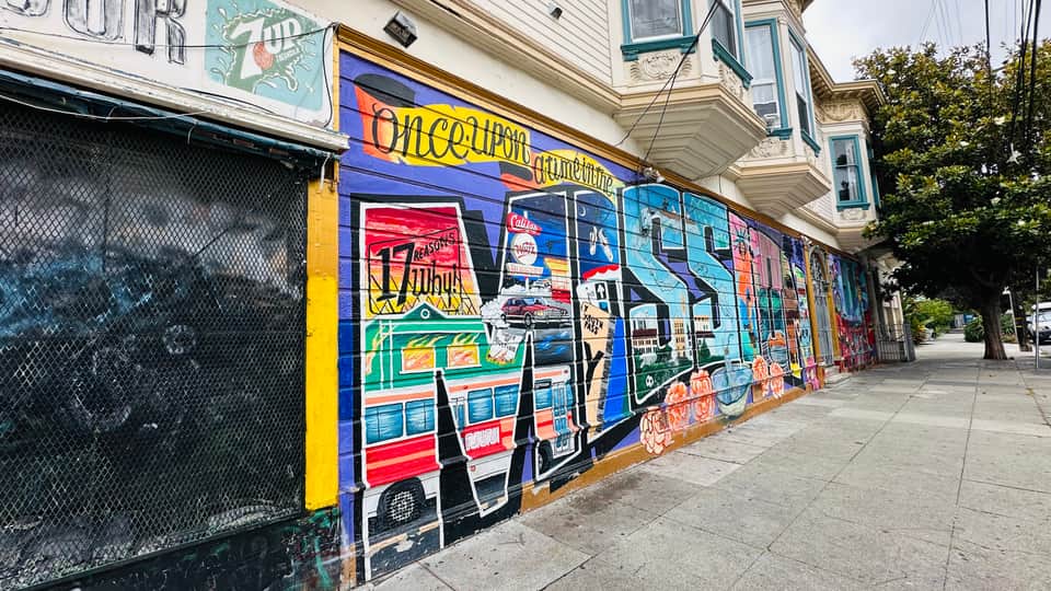 A muralled corner Victorian on Valencia Street in San Francisco's Mission District, with a row of Victorian facades receding up the block.