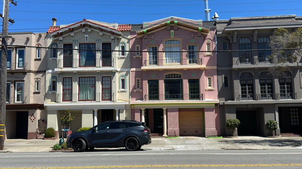 A row of pastel Edwardian flats in pink, grey and cream, each with its own entrance and garage.