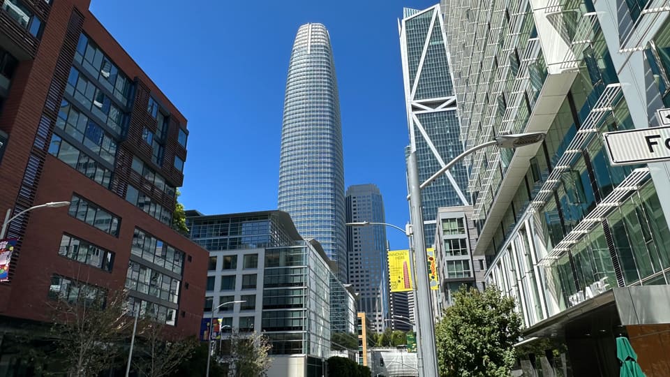 Salesforce Tower rising between a brick residential block and a glass facade on a South of Market street.