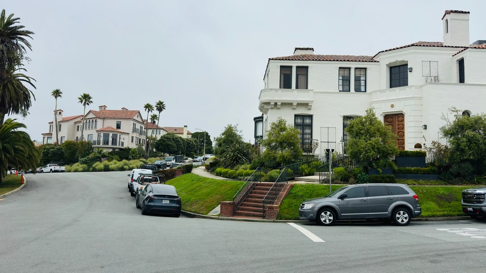 White Mediterranean-style houses with palms along a curved Sea Cliff street, cars parked at the kerb.
