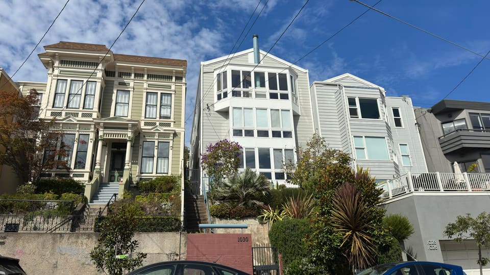 Two bay-windowed Victorians in cream and white side by side above stepped front entrances.