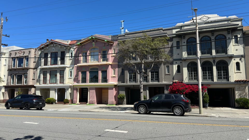A quiet SoMa block of garages and low flats climbing away from the camera, street trees along one side.