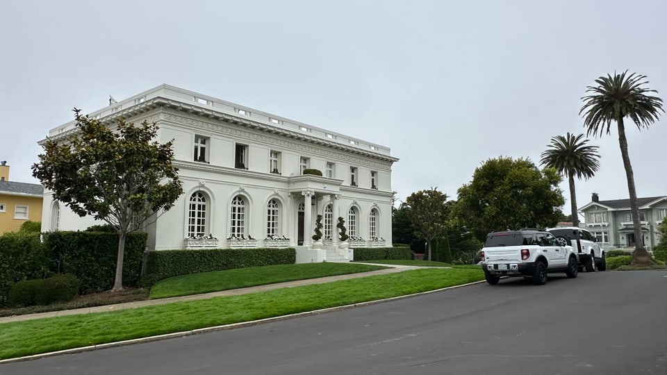 A white neoclassical mansion set back behind a lawn and palm on a quiet Presidio Heights street.