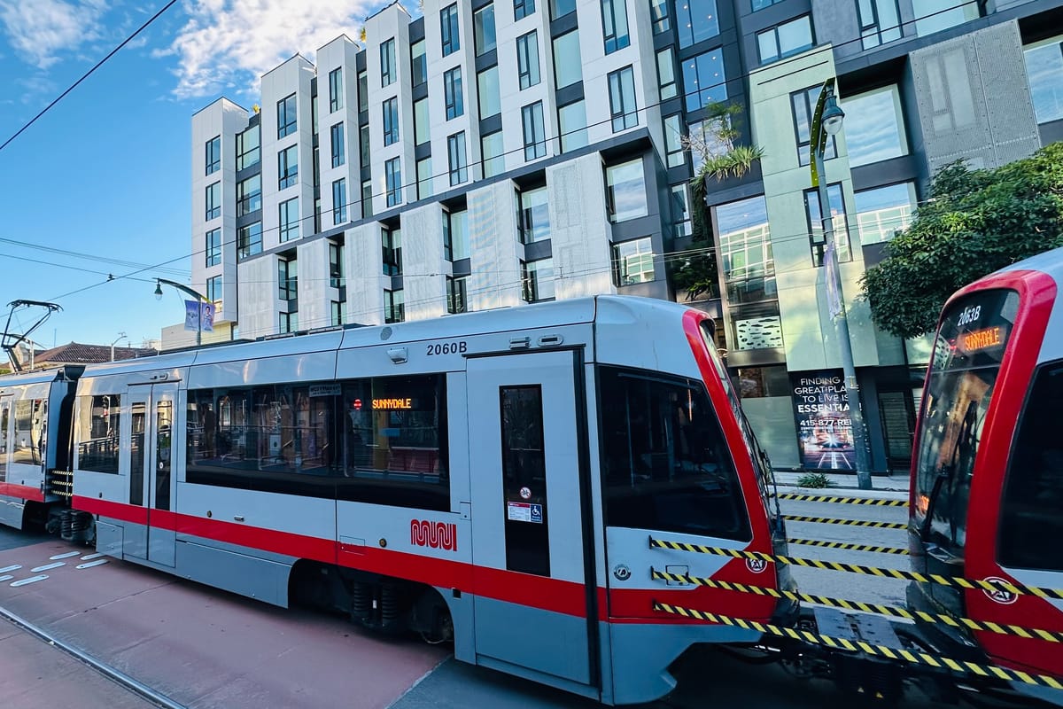 A Muni T-Third light rail train on Third Street in San Francisco's Mission Bay, with the neighborhood's mid-rise apartment buildings behind.