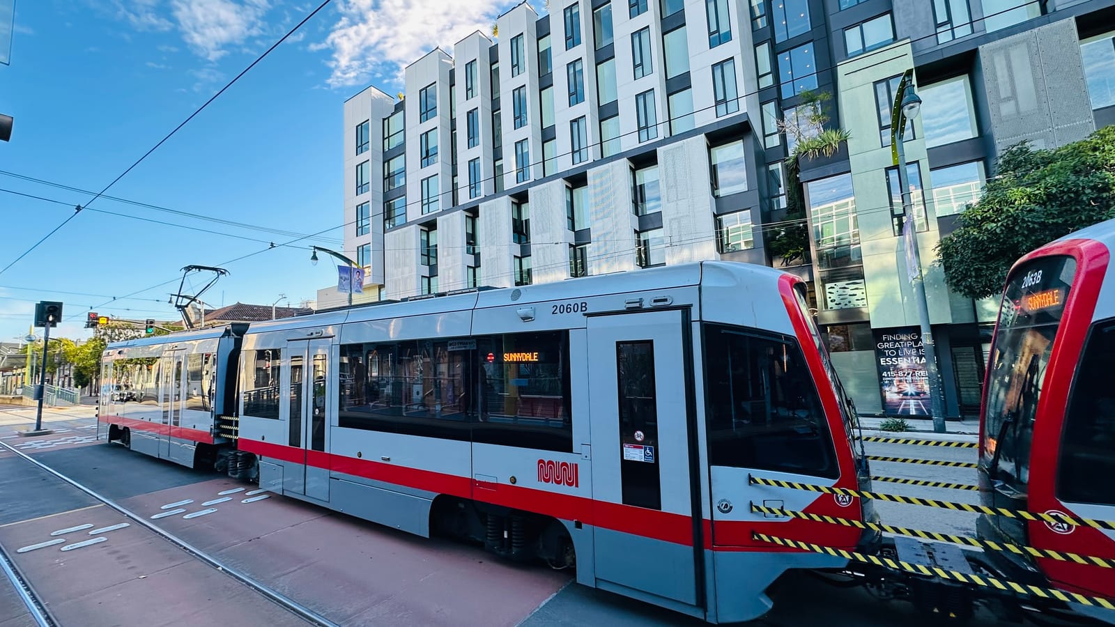 A Muni T-Third light rail train on Third Street in San Francisco's Mission Bay, with the neighborhood's mid-rise apartment buildings behind.
