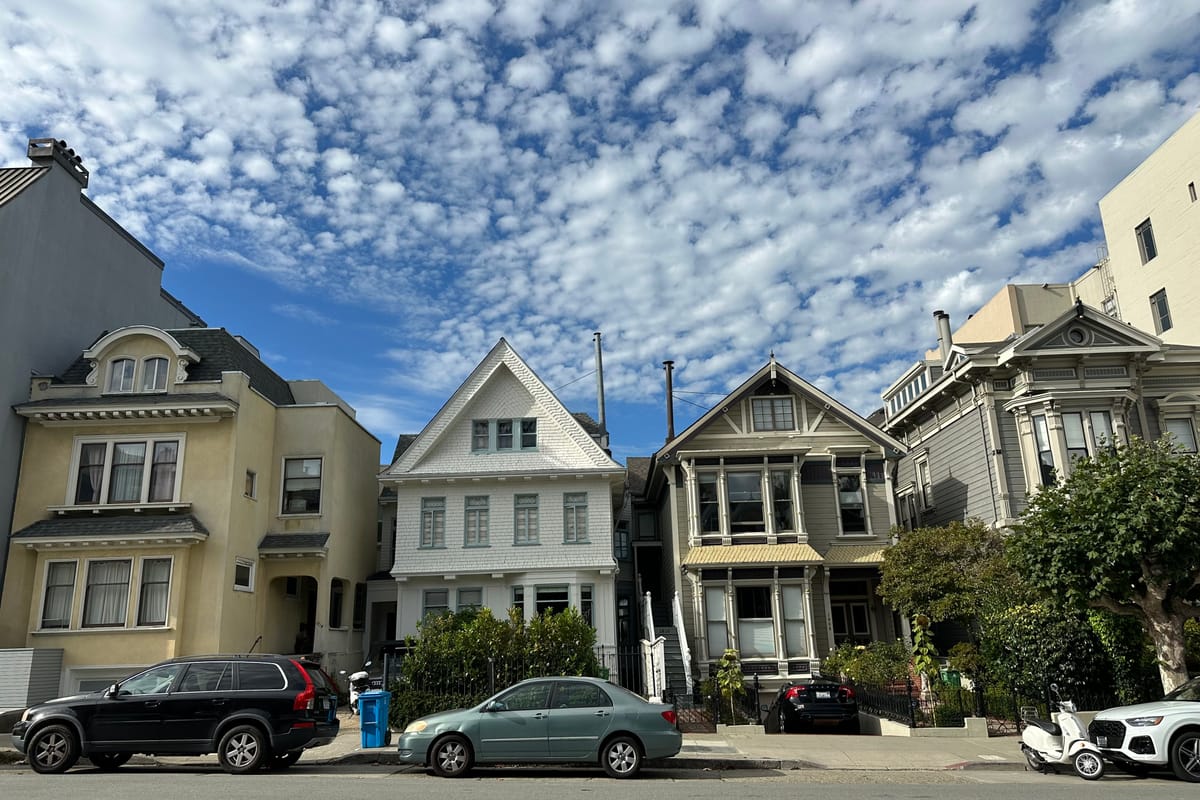 A row of pastel Victorian and Edwardian houses on a Pacific Heights hillside street in San Francisco, beneath a mackerel sky.