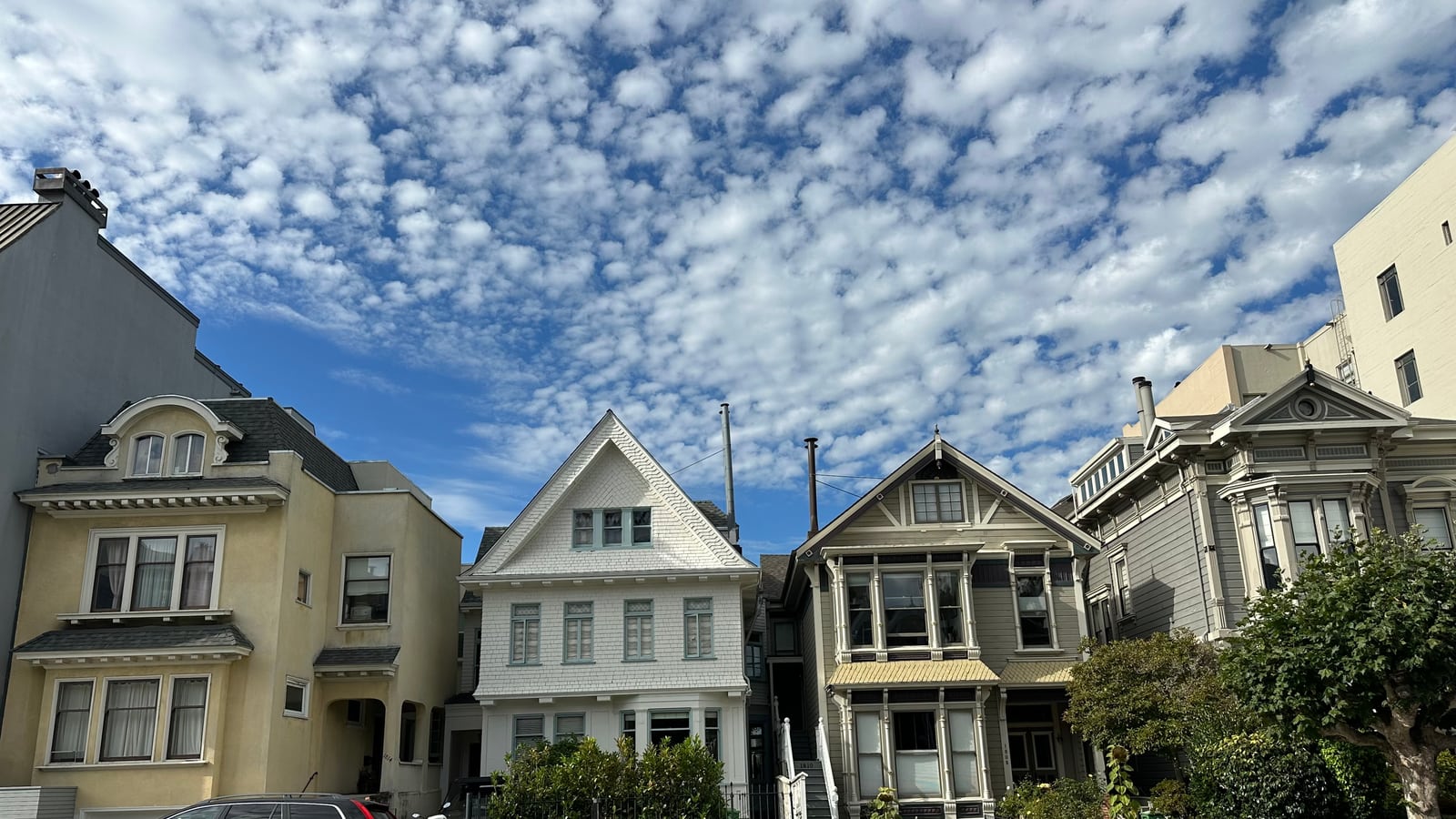 A row of pastel Victorian and Edwardian houses on a Pacific Heights hillside street in San Francisco, beneath a mackerel sky.